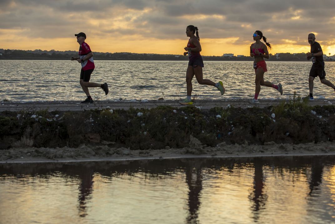Corredores en silueta contra la puesta de sol, reflejados en las salinas de Formentera